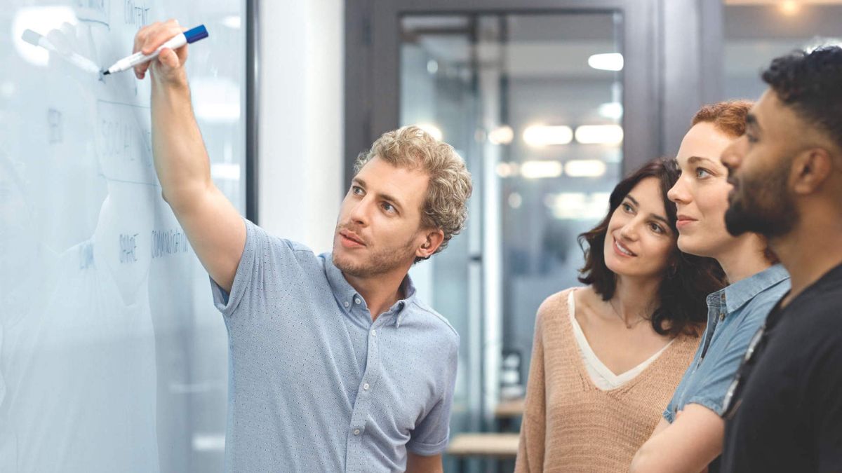 Businessman leading presentation at whiteboard. Young entrepreneur explaining the business plan to colleagues. They are in board room at office.