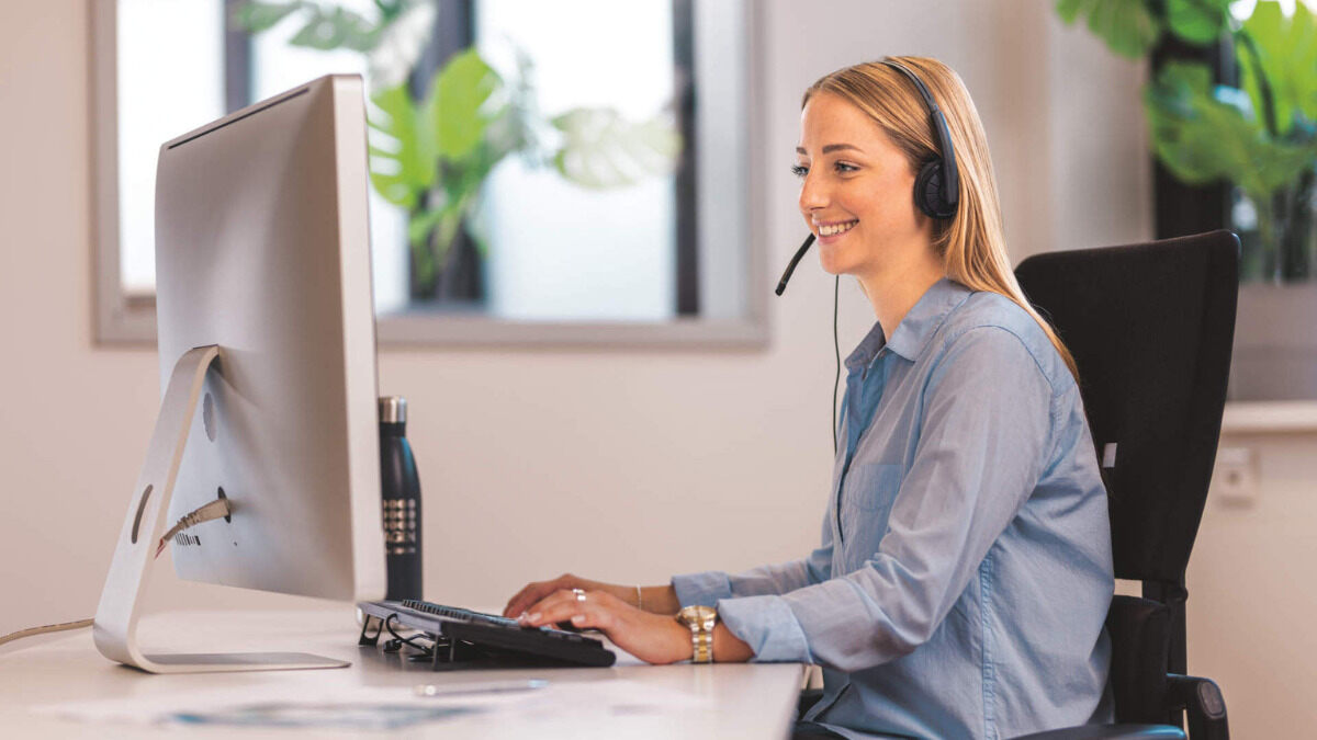 customer support, female sitting at computer with headset talking and positive expression