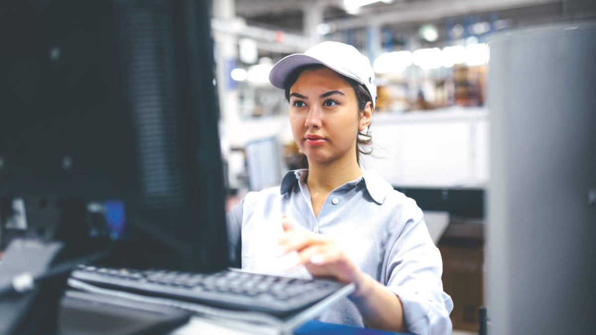 A young female worker/engineer works at her computer monitor in the factory