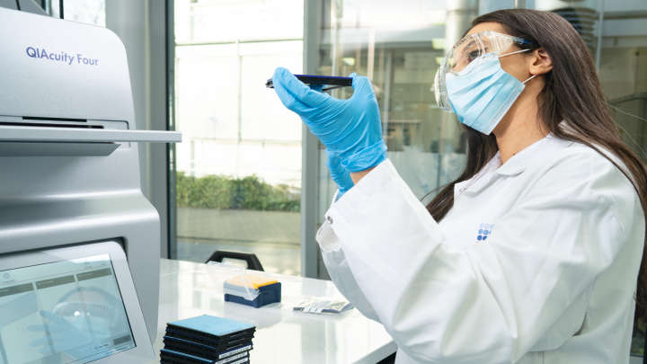 Labworker loading plate into the instrument, handling, wearing protection glasses and mask