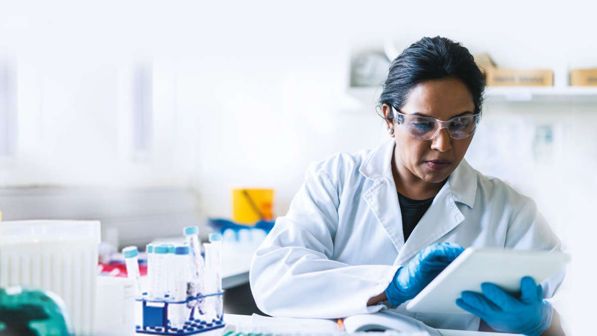 A woman in a lab coat in a lab looking at a tablet