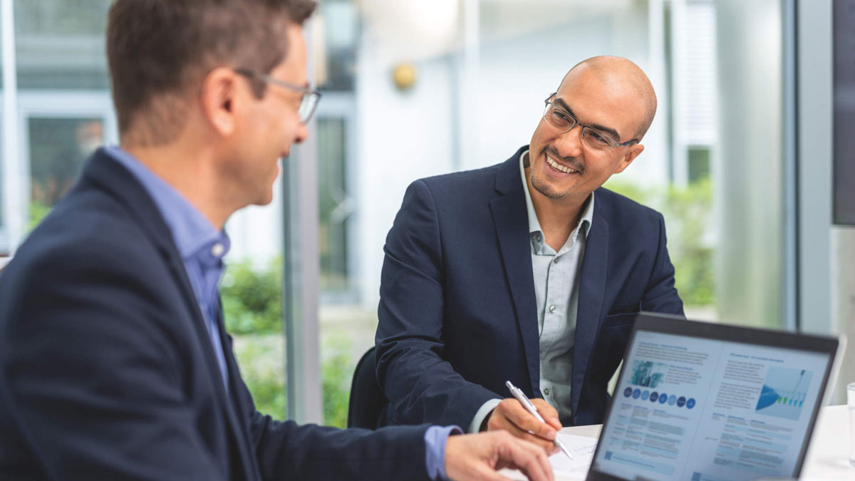 OEM, Generic, 2 males sat at table with positive expression, signing paper and at a computer