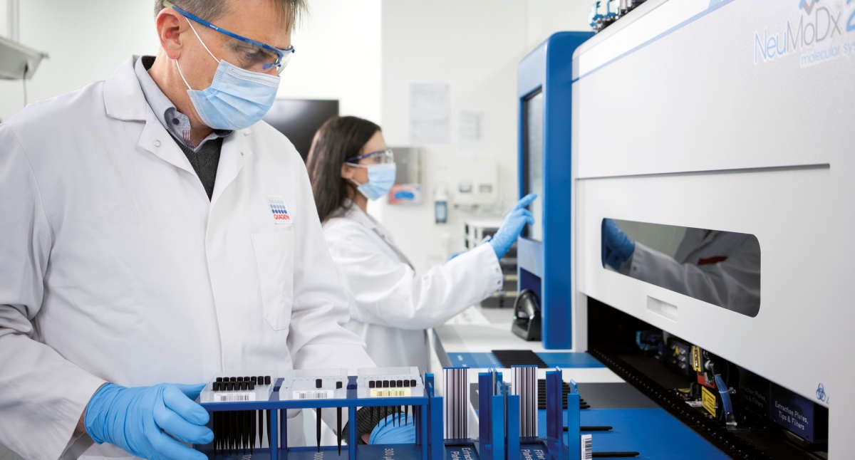 NeuMoDx, Labworker handling the instrument, loading tips, Julian Phillips, Chaimae Safi, mask, wearing masks, labcoat