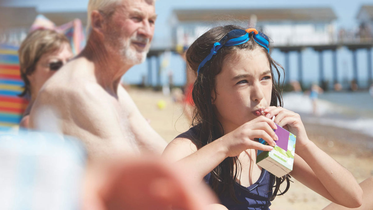 young girl drinking juice box on a beach