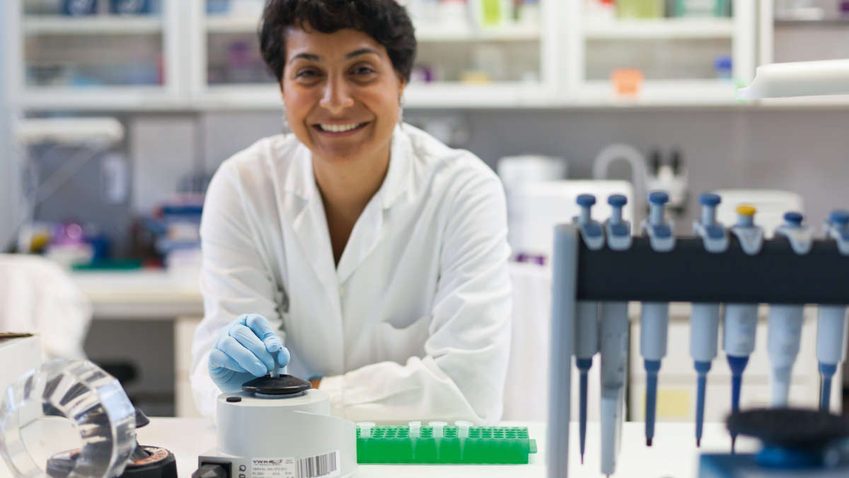 female Scientist working in a lab, laboratory environment, pipette in foreground, spin centrifuge